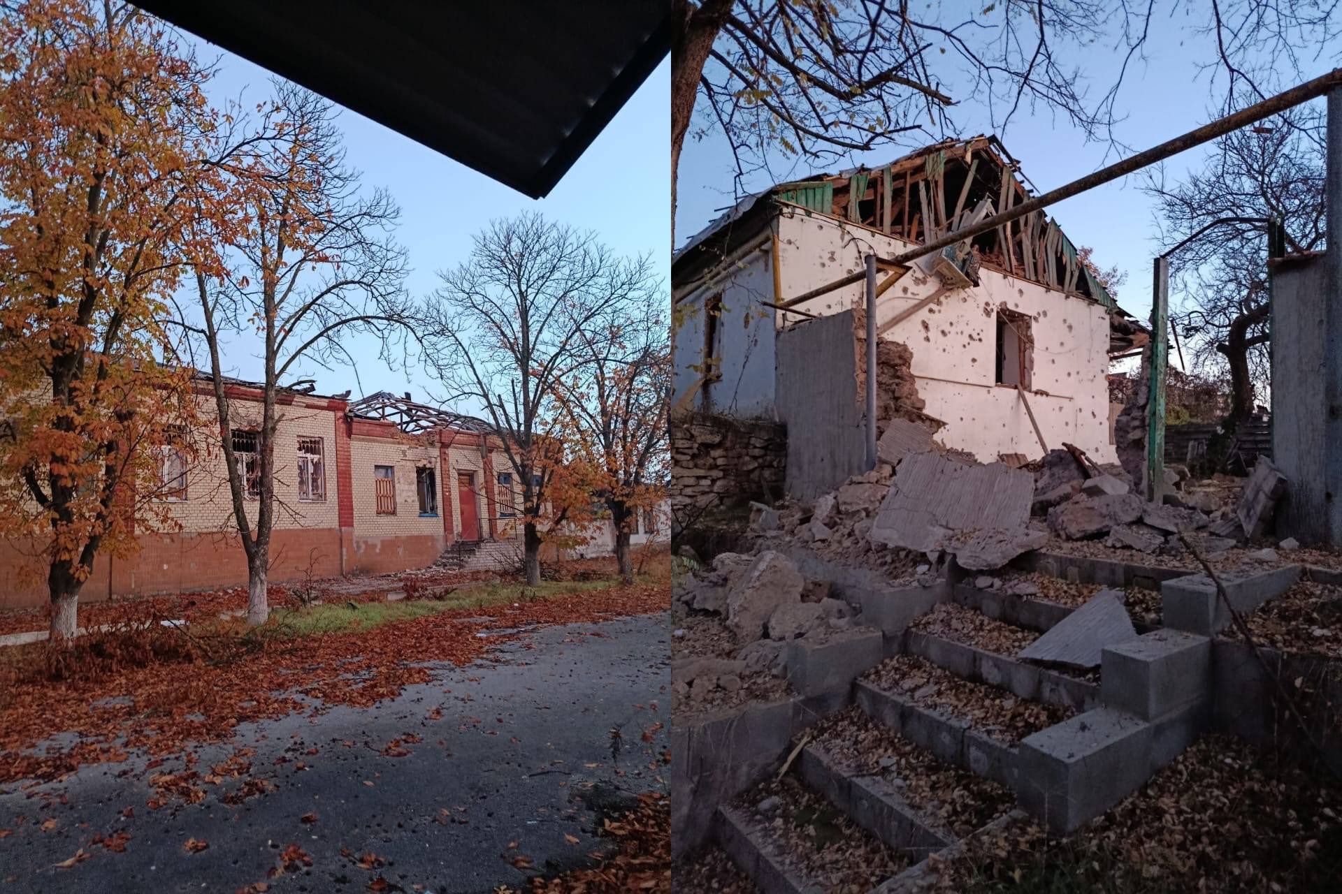 Дві зруйновані будівлі в осінньому пейзажі з опалим листям; одна цегляна будівля ліворуч, інша — сильно пошкоджена хата праворуч.