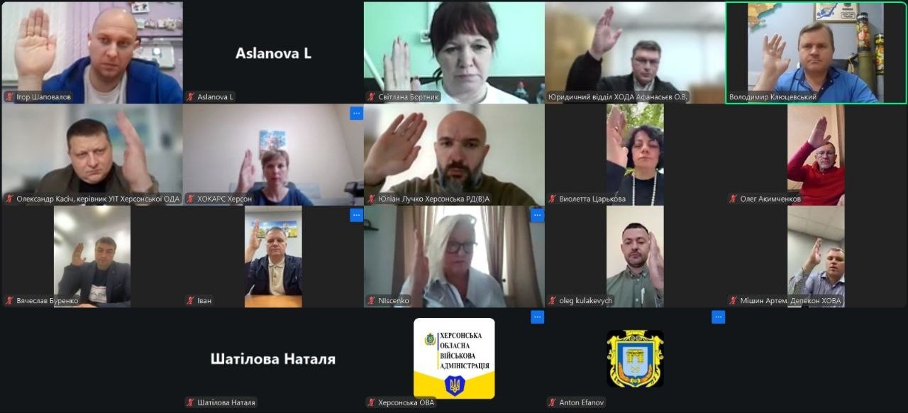 Скриншот онлайн-наради у форматі відеоконференції, на якому зображено сітку з вікнами численних учасників. Більшість присутніх тримають піднятою праву руку, що вказує на процес голосування або підтвердження рішення. Серед підписів до вікон видно імена посадовців та назви підрозділів