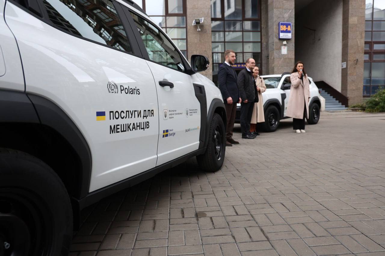 Крупний план білого позашляховика моделі Polaris, припаркованого на брукованій площі біля офісної будівлі. На борту автомобіля розміщений логотип Polaris та великий напис