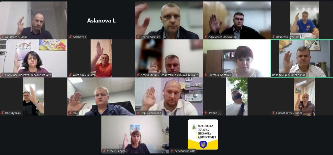 Скриншот онлайн-наради в додатку Zoom, інтерфейс якого розділений на сітку з вікон учасників. У більшості вікон зображені спікери — чоловіки та жінки, які підняли праву руку вгору під час голосування. Одне з вікон у правому верхньому кутку підсвічене зеленою рамкою та підписане «Володимир Клюцевський». Серед інших підписів присутні: «Царькова Віолетта Херсонська ОВА», «Артем Мішин. Департамент економіки ХОВА», «Олег Акимченков», «Ігор Шаповалов». Одне з вікон у нижньому ряду займає офіційна жовто-блакитна заставка з гербом та написом «ХЕРСОНСЬКА ОБЛАСНА ВІЙСЬКОВА АДМІНІСТРАЦІЯ».
