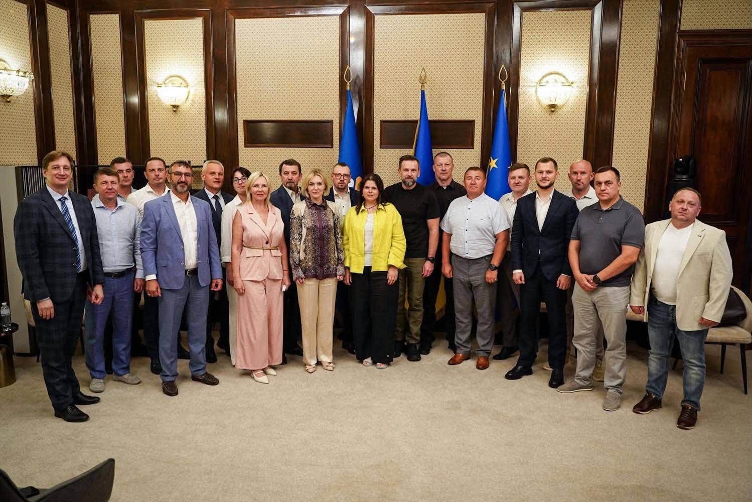 Спільне групове фото учасників засідання в офіційній залі. Понад 20 посадовців, серед яких заступник Керівника Офісу Президента, народні депутати, голови ОВА та представники місцевого самоврядування, вишикувалися в один ряд на тлі прапорів України, ЄС та Конгресу.