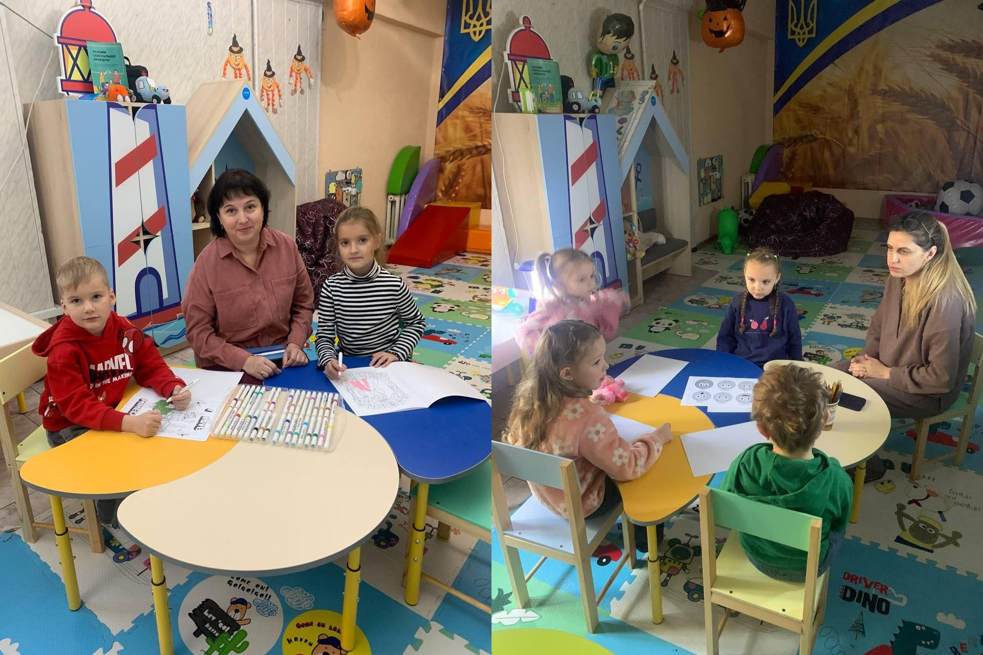 Це зображення є колажем із двох фотографій, зроблених у дитячому ігровому та навчальному центрі. На лівому фото жінка та двоє старших дітей (хлопчик у червоному та дівчинка у смугастому светрі) сидять за столом, малюють і посміхаються. На правому фото інша жінка сидить із трьома молодшими дітьми за круглим столом; діти також малюють. Кімната яскраво прикрашена: видно іграшки та українські прапори та символіку на стінах (Тризуб на синьо-жовтому тлі).
