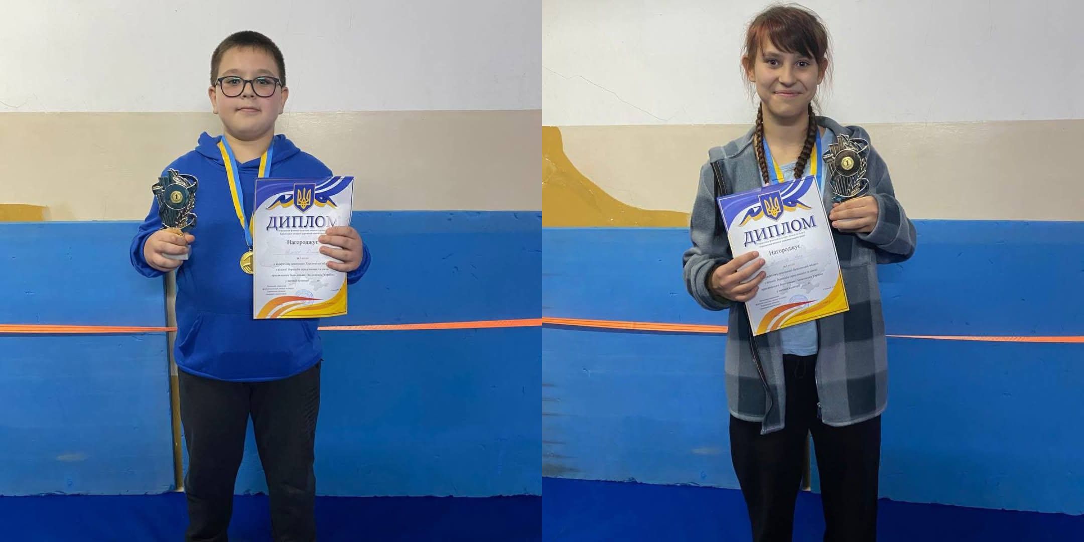 Складене фото, що зображує двох юних переможців змагань. Ліворуч: Хлопчик у синій кофті та окулярах, з медаллю на жовто-блакитній стрічці, тримає в руках кубок та диплом (з написом "ДИПЛОМ" та зображенням українського герба). Праворуч: Дівчинка у картатій сорочці, з медаллю на жовто-блакитній стрічці, тримає в руках кубок та диплом. Обидва стоять на фоні, схожому на стіну спортивного залу, пофарбовану в світлий колір та синій знизу, дивлячись у камеру.