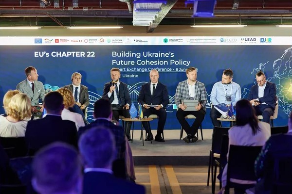 Спікери сидять на сцені під час офіційної конференції, присвяченої європейській політиці згуртованості України, перед аудиторією в залі.