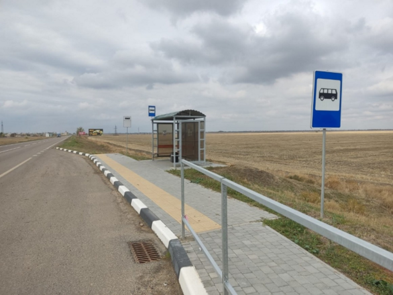 Автобусна зупинка на узбіччі заміської траси посеред порожнього поля під хмарним небом.