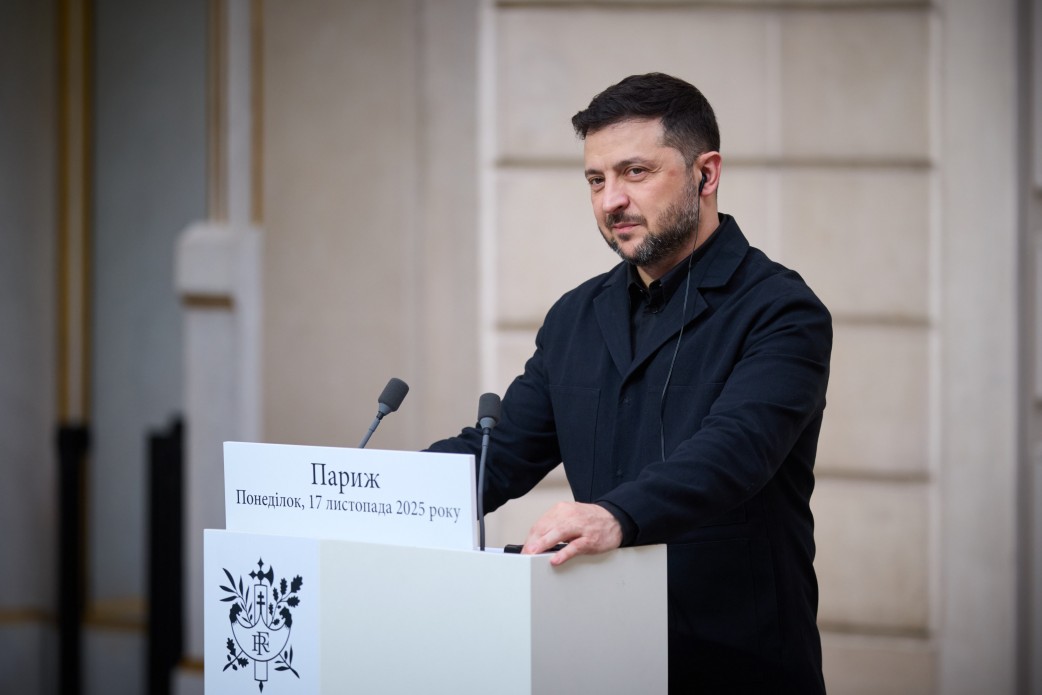 Президент Володимир Зеленський у чорному одязі стоїть за трибуною під час виступу. На табличці перед ним написано: Париж, Понеділок, 17 листопада 2025 року
