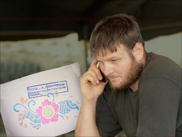 Чоловік з бородою, сидить, говорить по мобільному телефону, притискаючи його до вуха. Перед ним видно частину аркуша паперу або конверта з квітковим візерунком та офіційною печаткою.