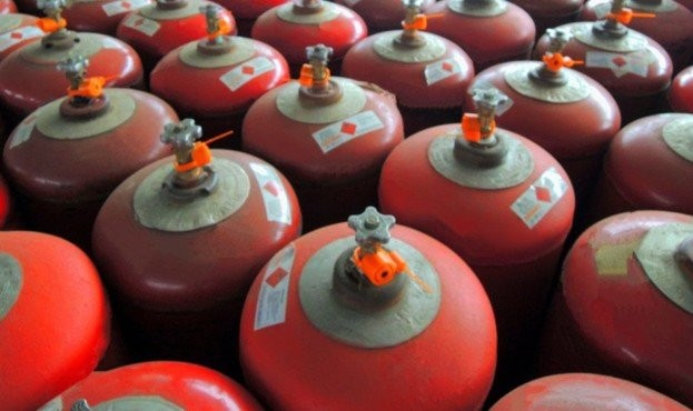 Червоні циліндричні балони високого тиску з вентилями та попереджувальними наклейками, розташовані близько один до одного, заповнюючи кадр.