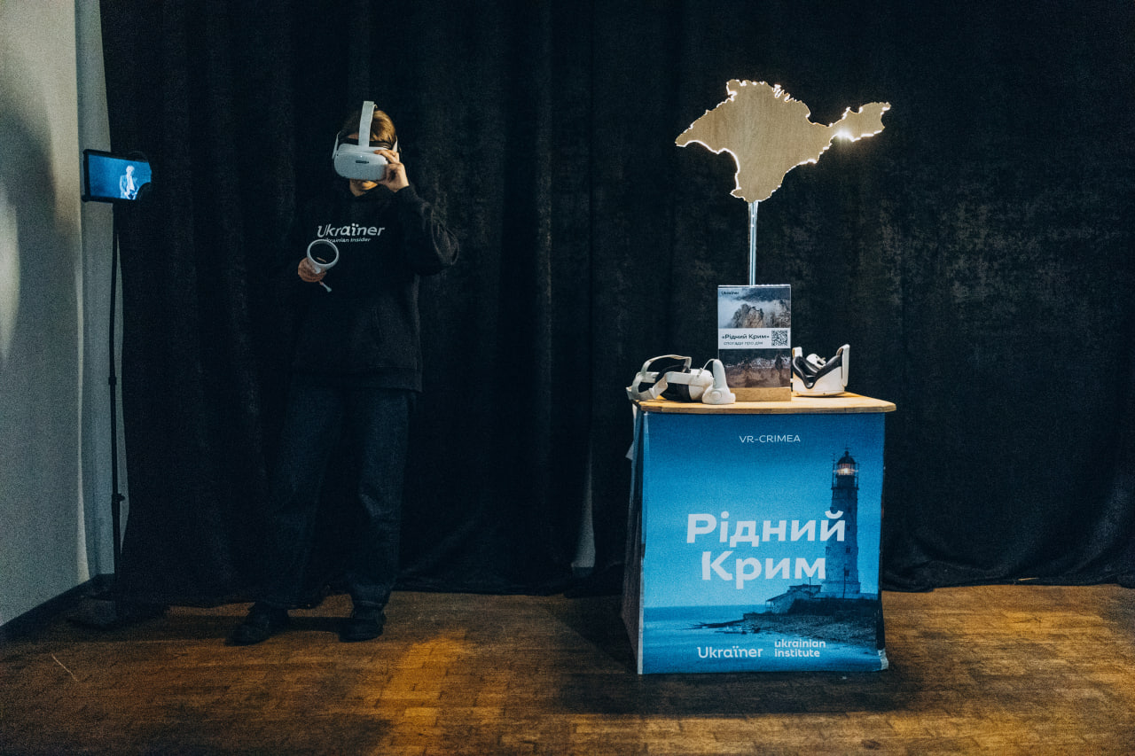 Локація з віртуальною реальністю на виставці: людина у VR-шоломі тестує обладнання поруч із банером «Рідний Крим» та підсвіченою дерев'яною картою Криму.