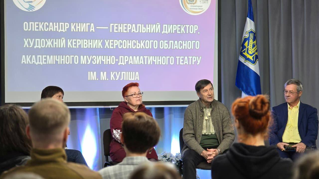 Панельна дискусія. Четверо людей сидять перед аудиторією. На екрані позаду них великим шрифтом відображено: 