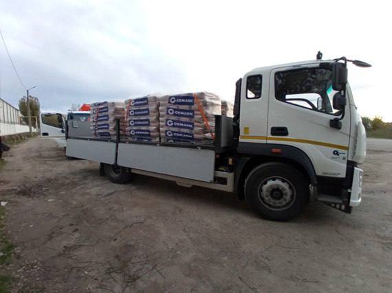  Вантажний автомобіль білого кольору, з відкидними бортами, завантажений багатьма мішками з цементом або будівельною сумішшю з логотипом 