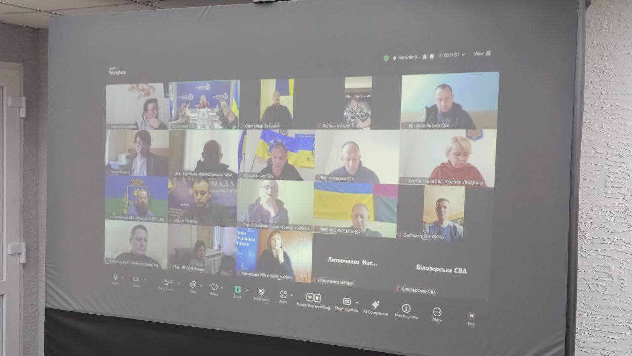 Це фотографічний знімок екрана, на якому видно сітку учасників онлайн-конференції (ймовірно, Zoom). Більшість учасників — це люди, які сидять перед камерами, а деякі мають підписані назви організацій та громад.