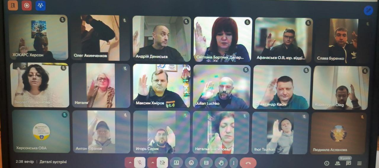 Екран відеоконференції (вірогідно, Google Meet) з 18 учасниками, більшість з яких підняли праві руки. Відображаються їхні імена та посади.