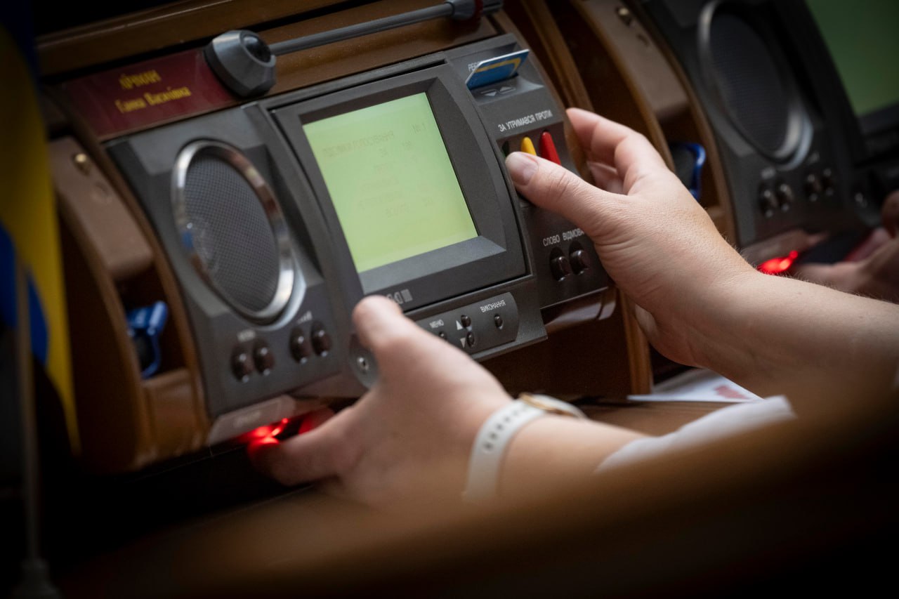 Крупний план рук, що взаємодіють із електронною системою для голосування або конференцій (ймовірно, в парламенті чи на засіданні).