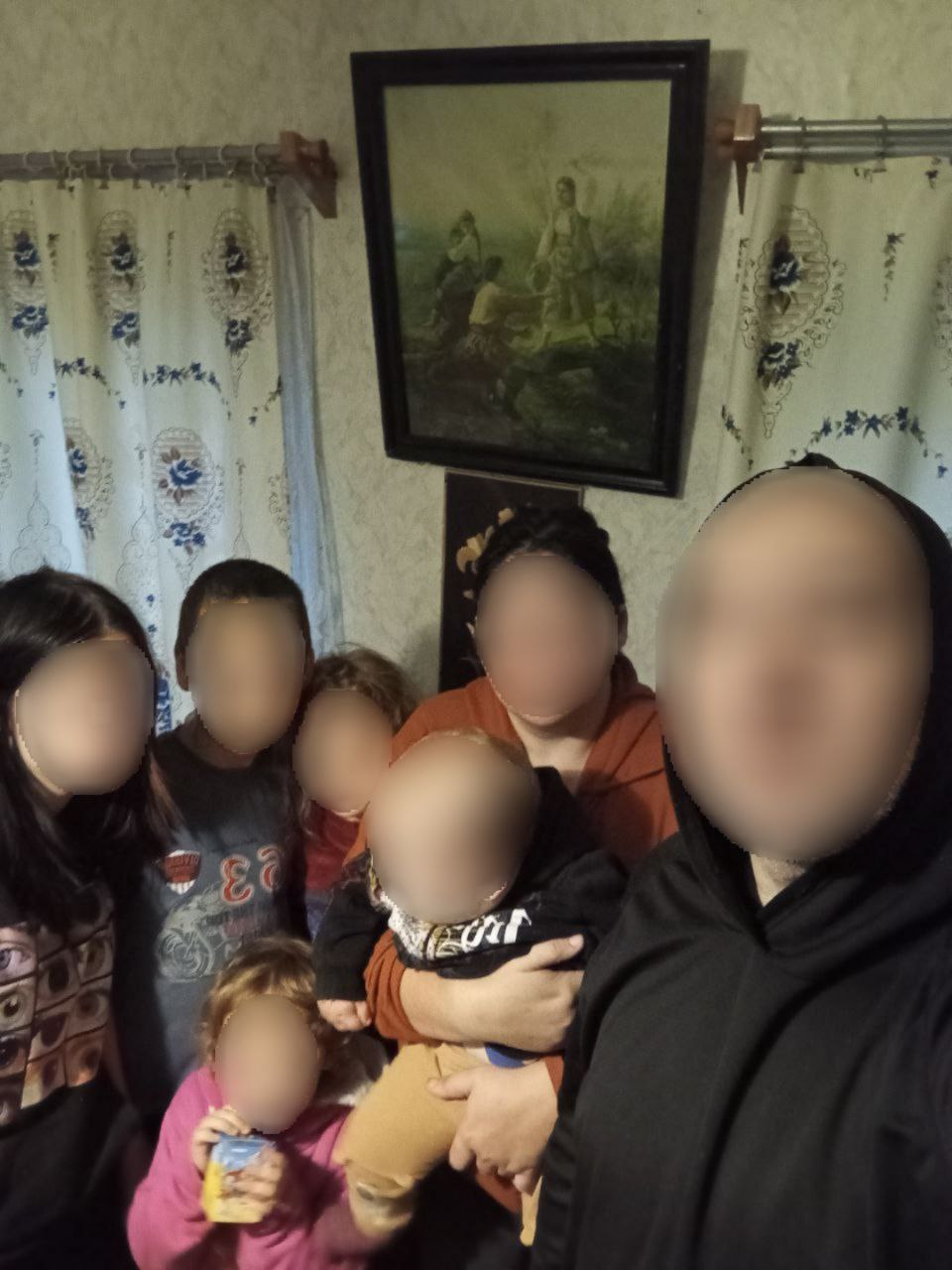 Груповий портрет великої родини (сім'я з кількома дітьми та дорослими) у приміщенні з картиною та шторами на задньому плані.