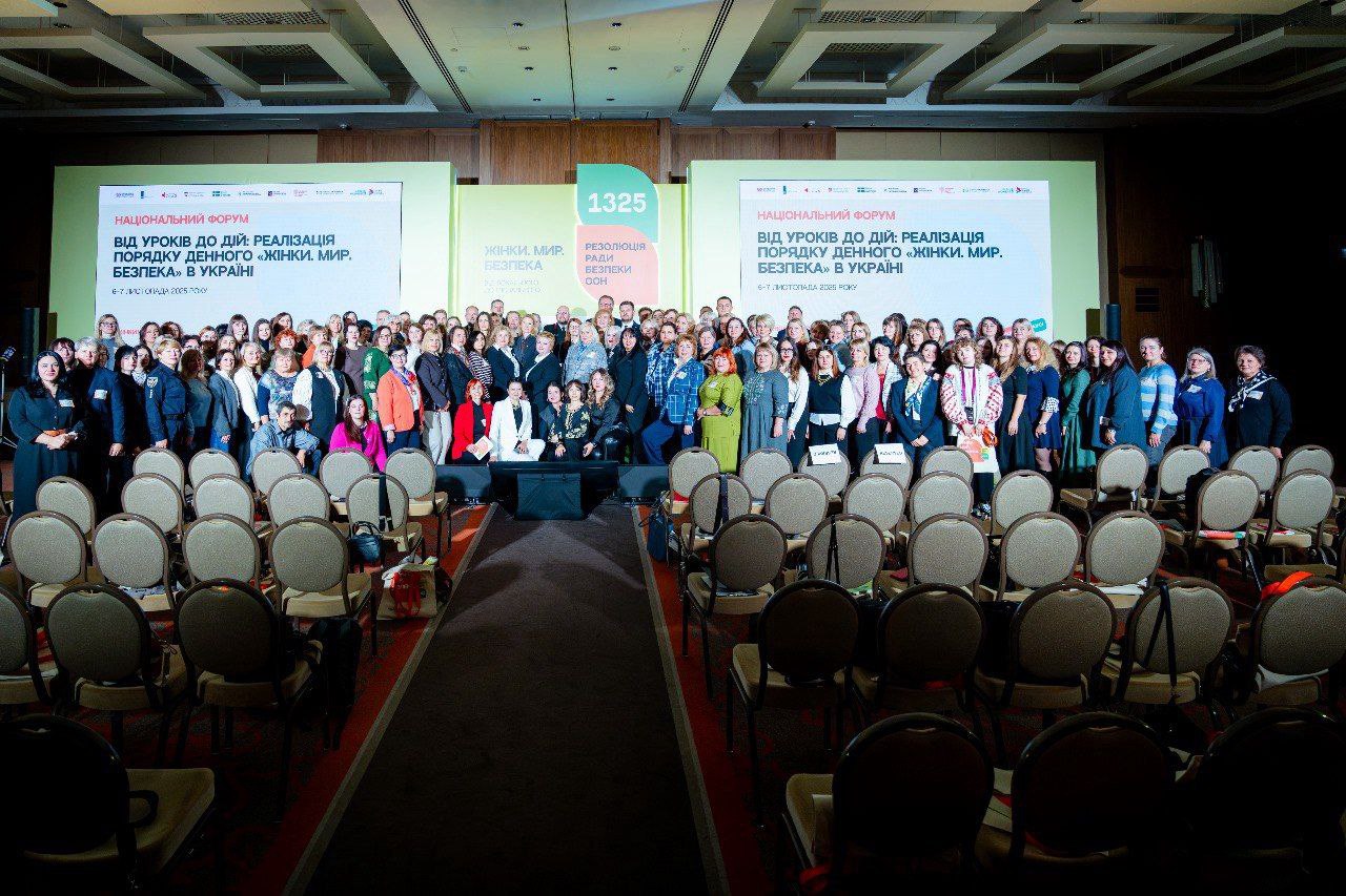 Кругове фото великої групи людей (переважно жінок) на сцені та перед нею на Національному форумі в Україні. На екранах позаду видно напис: Від уроків до дій: реалізація порядку денного Жінки, мир, безпека» в Україні.