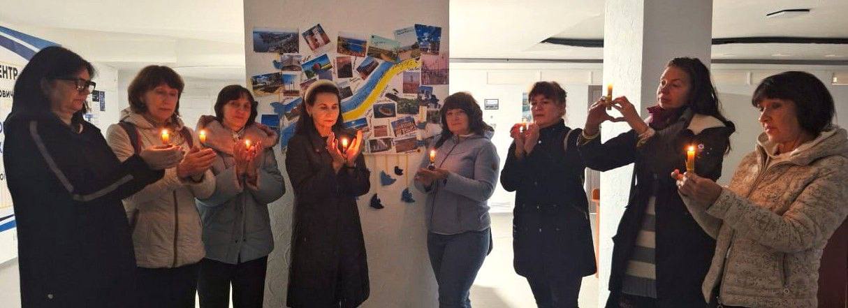 Вісім жінок у приміщенні стоять у ряд, тримаючи в руках запалені свічки, під час церемонії  вшанування пам'яті тих людей, яких Херсонщина втратила під час окупації та тих, хто віддав життя за свободу рідного краю.