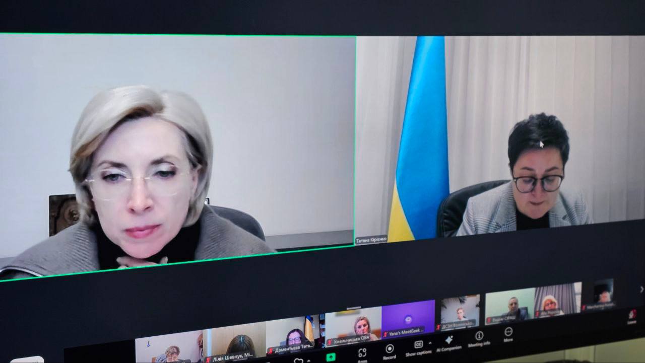 Дві жінки - учасниці онлайн-конференції (Zoom), на екрані комп'ютера. Ліворуч — світловолоса жінка в окулярах, праворуч — темноволоса жінка в окулярах, позаду неї видно прапор України.