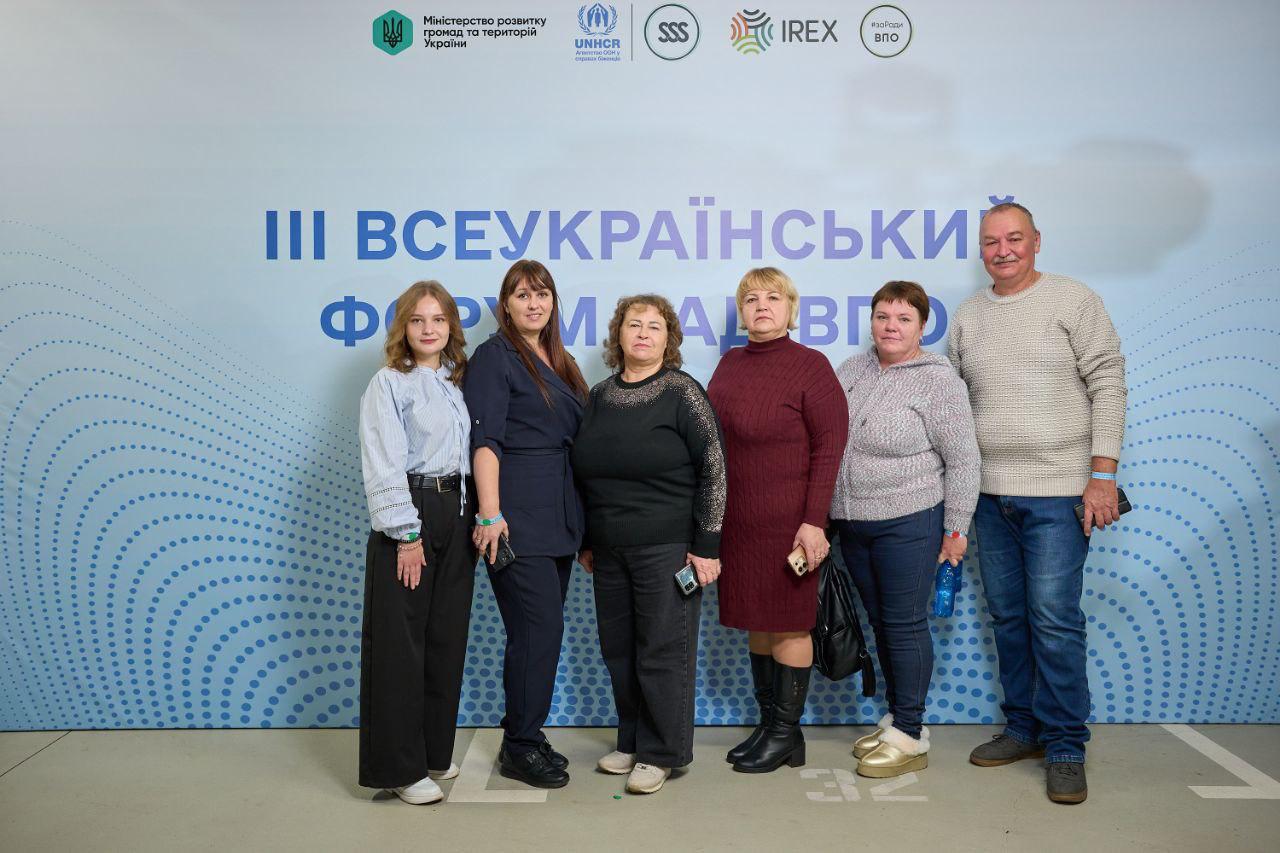 Шість людей (п'ять жінок і один чоловік) стоять разом і посміхаються на тлі банера з текстом: ІІІ Всеукраїнський Форум рад ВПО та логотипами, зокрема Міністерства розвитку громад і територій України, UNHCR та IREX.