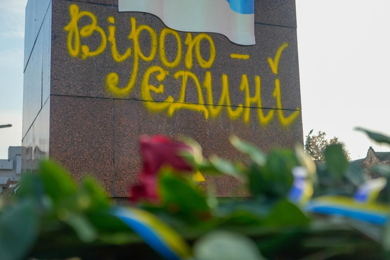 Крупний план монумента з жовтим написом: Вірою – Єдині та стилізованим українським прапором, перед яким лежать квіти та синьо-жовті стрічки.