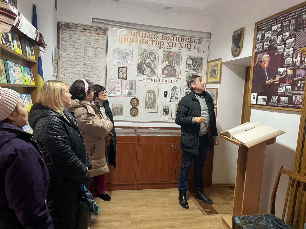 Група з чотирьох жінок та одного чоловіка стоїть у приміщенні музею, чоловік вказує на великий стенд зі світлинами та текстом про відому постать, поруч з яким розташований стенд про ГАЛИЦЬКО-ВОЛИНСЬКЕ КНЯЗІВСТВО XII-XIII ст.