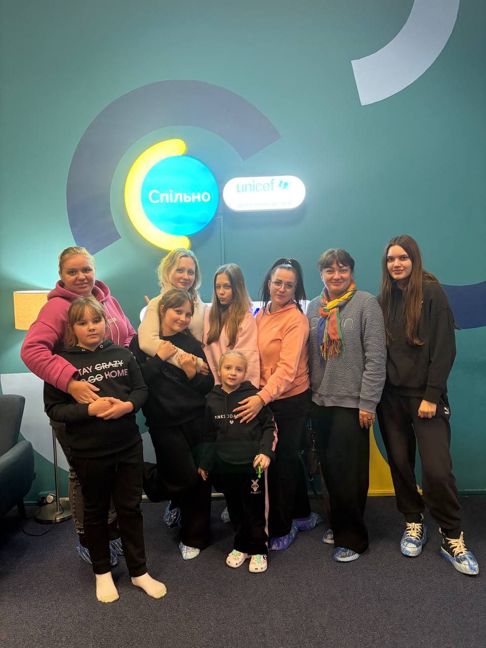 Групова фотографія восьми жінок та дівчаток, які стоять у приміщенні на тлі великого логотипу, що складається з написів: Спільно та unicef.