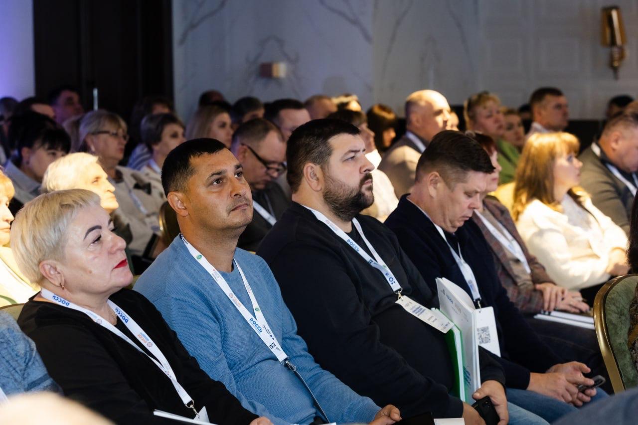 Група людей сидить в аудиторії, уважно слухаючи виступ на конференції чи обговоренні. Усі учасники мають на шиї бейджики, кілька з них – з логотипом DOCCU.