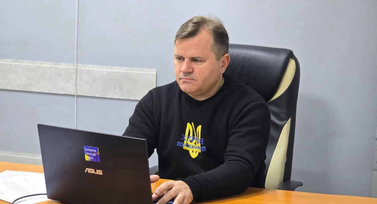 Чоловік у чорному светрі з українським Тризубом сидить за столом і зосереджено працює за ноутбуком.