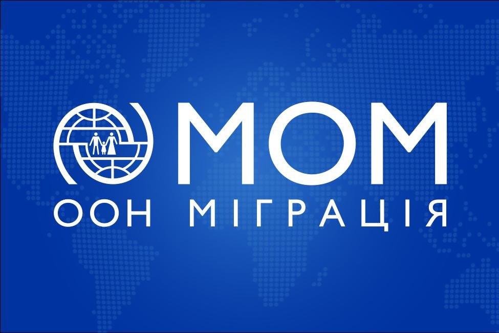 Логотип Міжнародної організації з міграції (МОМ) на синьому тлі з написом: ООН МІГРАЦІЯ.