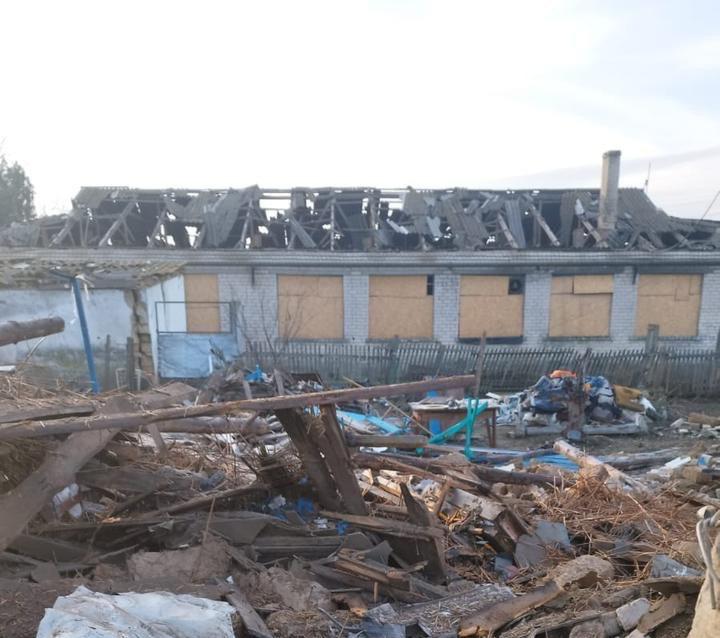 Зруйнована одноповерхова цегляна будівля зі знищеним дахом та вікнами, забитими фанерою, на передньому плані купа будівельного сміття та уламків.