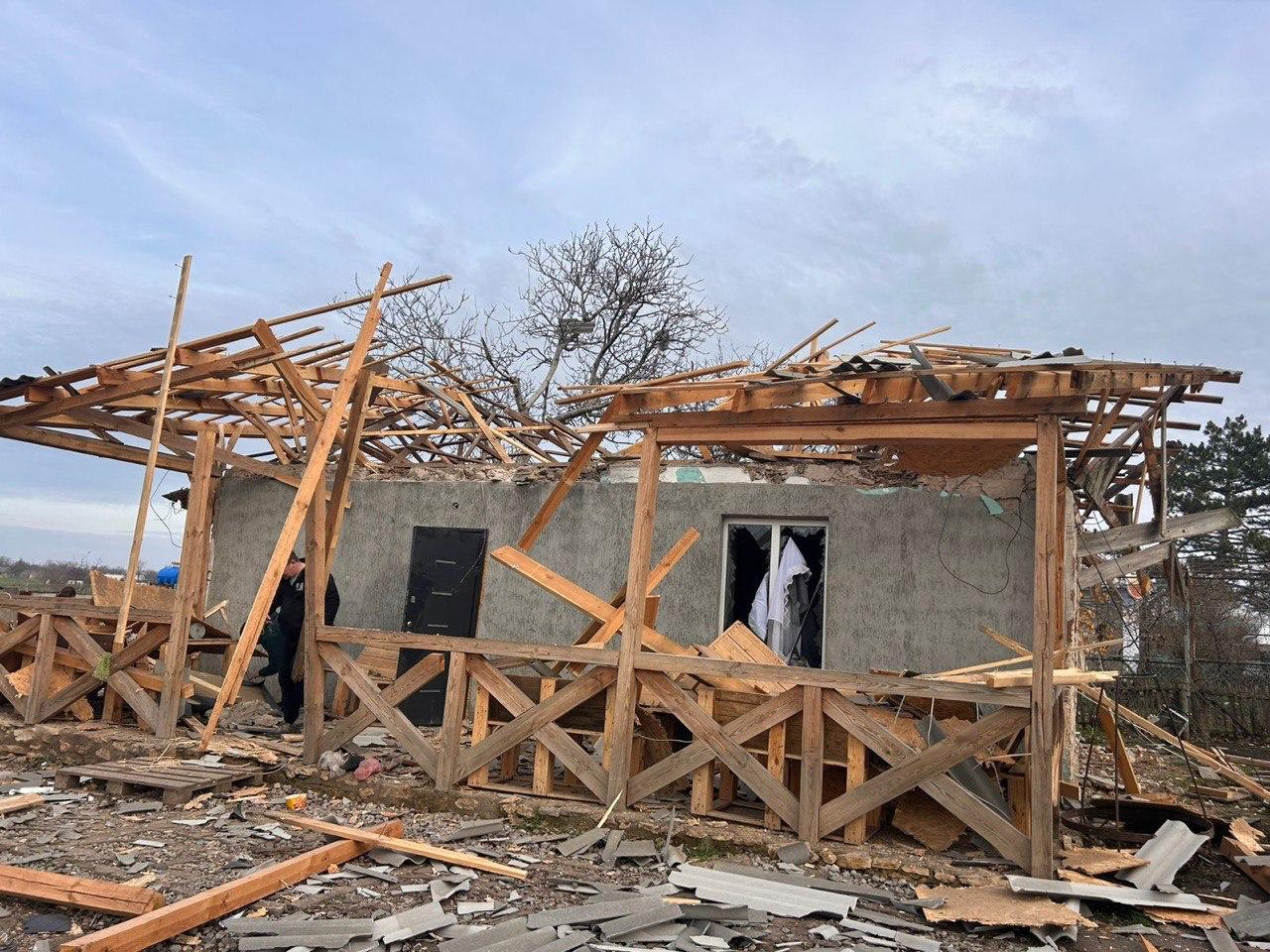 Зруйнований приватний будинок з пошкодженим дахом та дерев'яною верандою, частково знесеною вибухом. Навколо розкидані уламки дерева та шиферу.