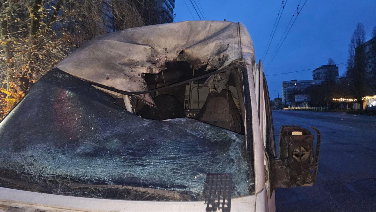 Крупний план сильно пошкодженого та обгорілого лобового скла та кабіни фургона в сутінках. Частина даху та тент над лобовим склом повністю обгоріли, саме скло розбите.