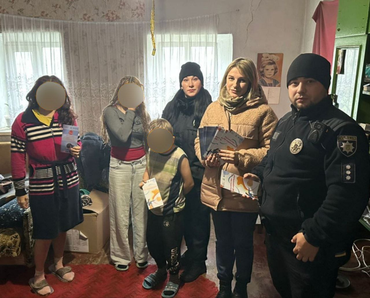Двоє поліцейських та троє цивільних (дві жінки та дитина) стоять у кімнаті, тримаючи в руках інформаційні листівки.