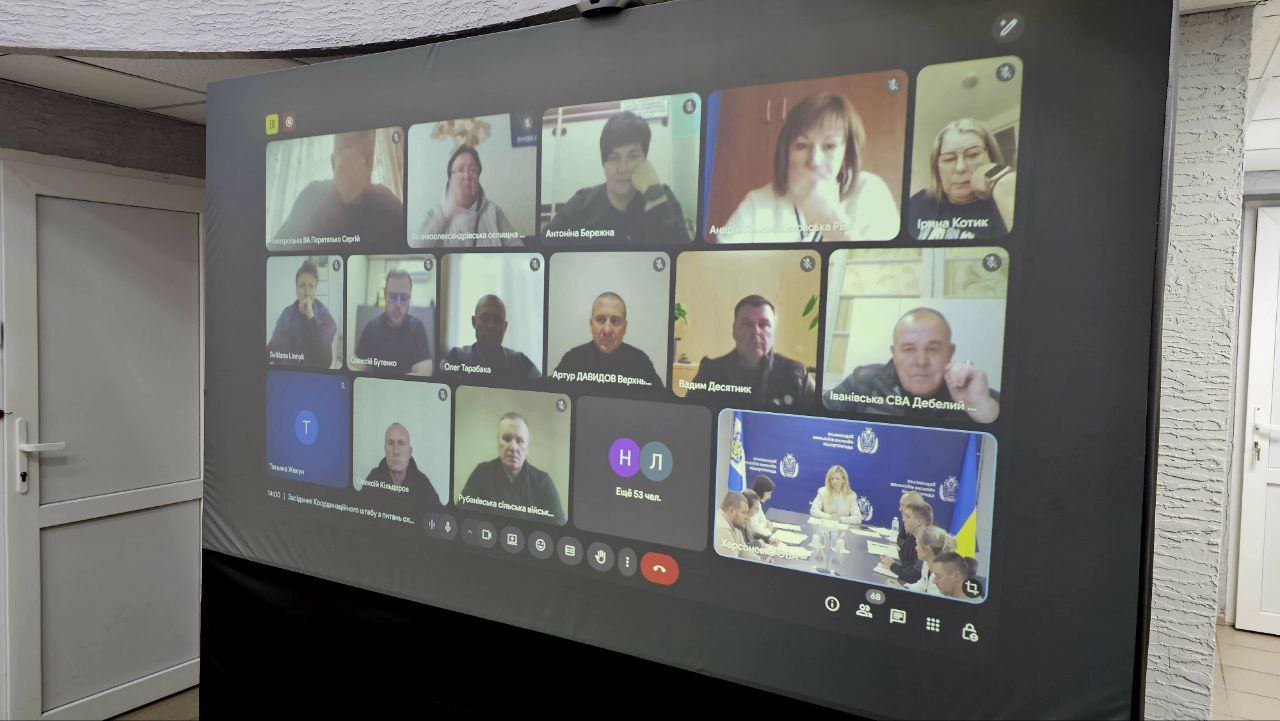 Відеоконференція (онлайн-зустріч) у додатку з 15 учасниками, чиї обличчя та імена (переважно кирилицею) відображаються у віконцях на великому проекційному екрані.