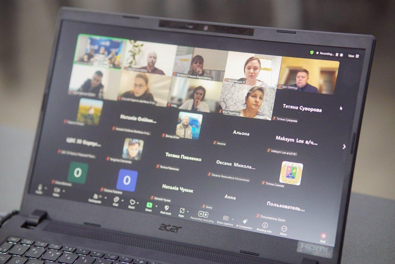 Екран ноутбука Acer демонструє відеоконференцію в Zoom, на якій видно сітку з вікнами численних учасників. Деякі вікна містять відеозображення людей, інші — імена або аватарки.