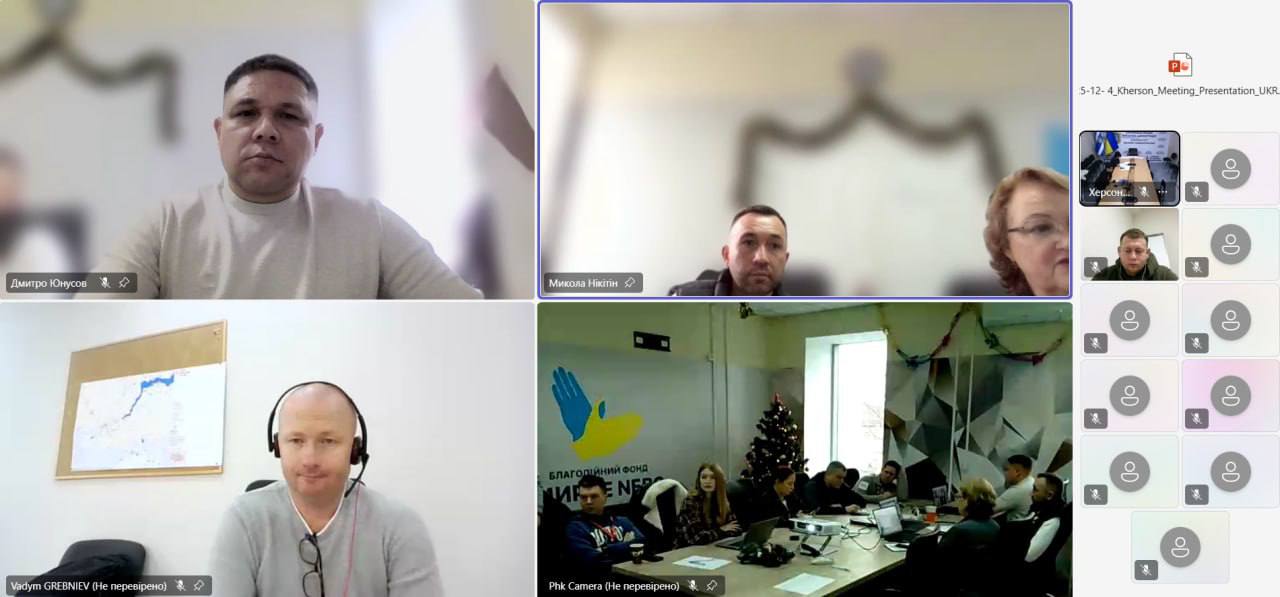 Крупний план учасників онлайн-зустрічі (чоловіків та жінки) на екрані відеоконференції, а також група людей, що сидять за столом у кімнаті з різдвяною ялинкою та банером фонду Мирне Небо.