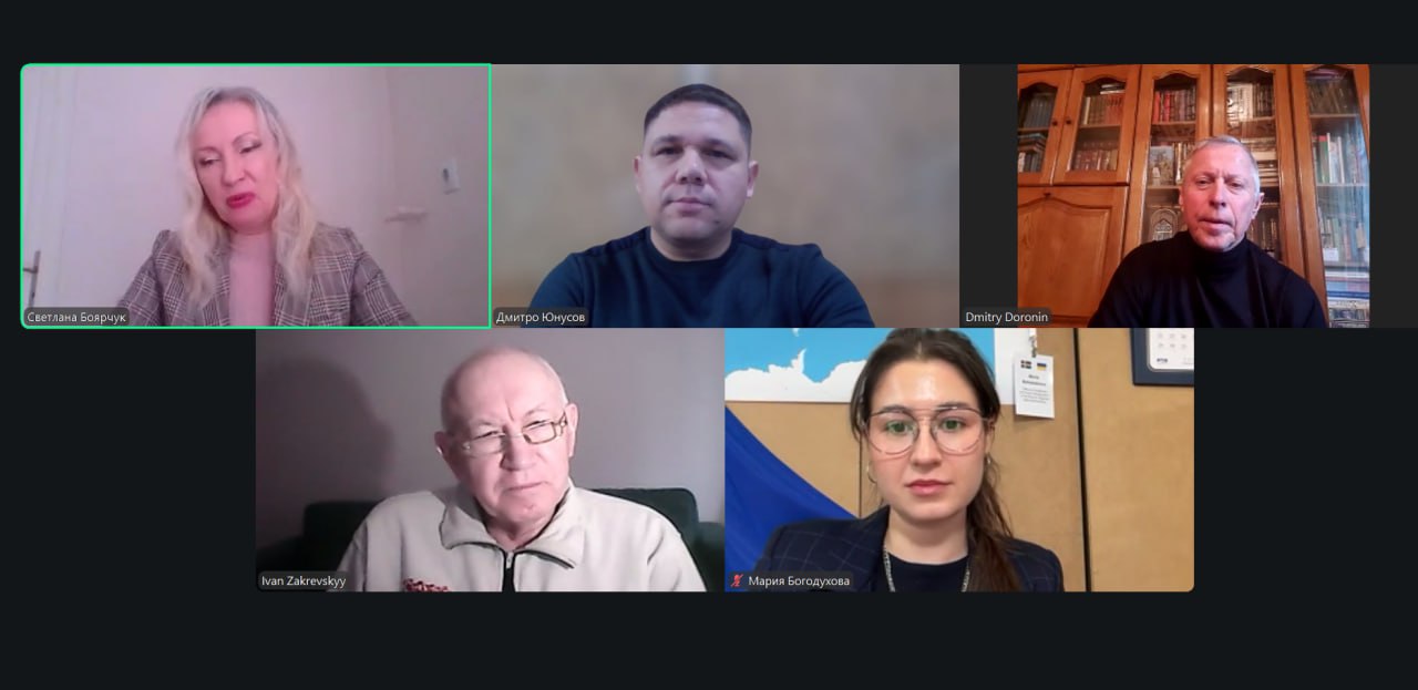 Скриншот відеоконференції, що демонструє п'ятьох учасників у п'яти вікнах: Верхній ряд (зліва направо): Жінка зі світлим хвилястим волоссям, у картатому піджаку. Літній чоловік у чорному светрі. Нижній ряд (зліва направо): Лисий чоловік в окулярах і білій сорочці. Чоловік з темним коротким волоссям, у темно-синьому светрі, на тлі книжкових полиць. Молода жінка в окулярах та темному піджаку, на тлі синьо-жовтого прапора.