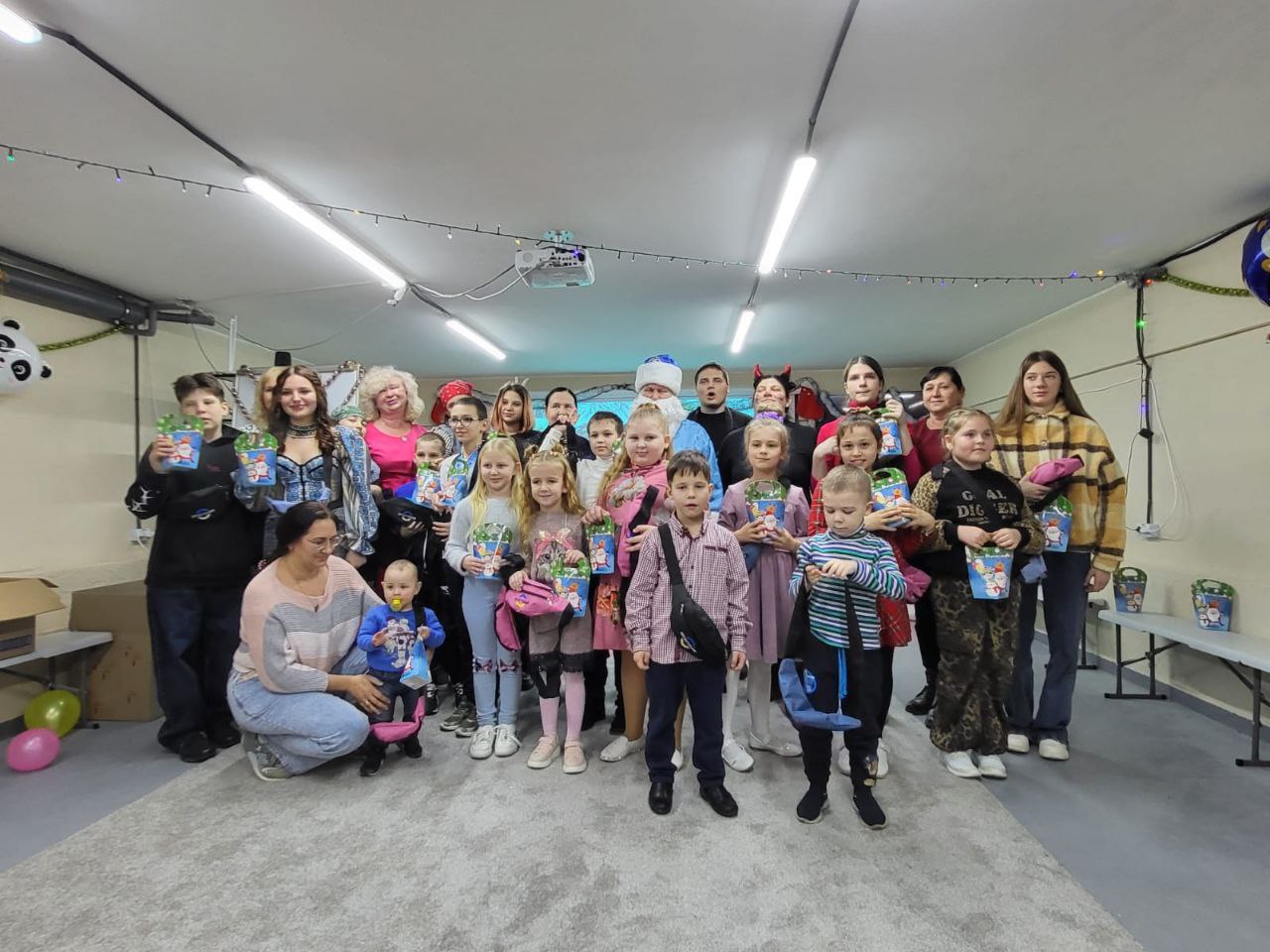 Груповий знімок дорослих та дітей у приміщенні під час святкування. У центрі стоїть чоловік у костюмі Святого Миколая. Діти тримають у руках подарункові кошики.