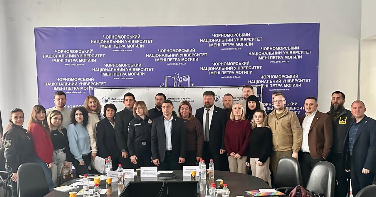 Група людей стоїть разом перед фіолетовим банером Чорноморського національного університету імені Петра Могили під час конференції.