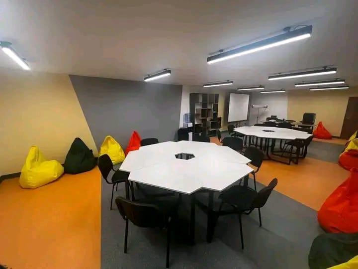 Сучасна кімната для нарад або коворкінгу зі стінами різних кольорів, двома великими багатокутними столами та м'якими кріслами-мішками жовтого, чорного та червоного кольорів.