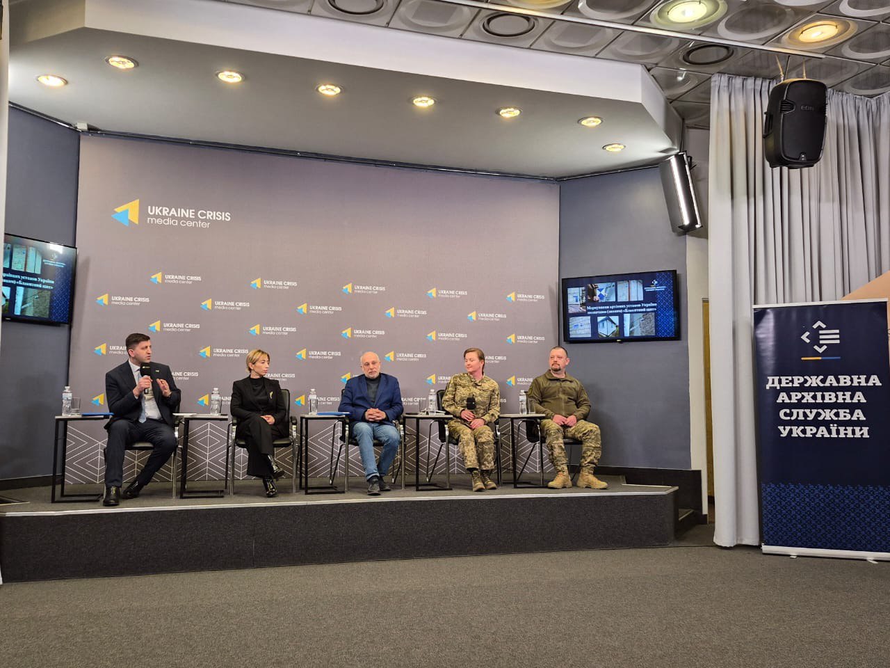 П'ятеро спікерів (троє у цивільному одязі та двоє у військовій формі) сидять на сцені під час пресконференції в Ukraine Crisis Media Center поруч із банером Державної архівної служби України.