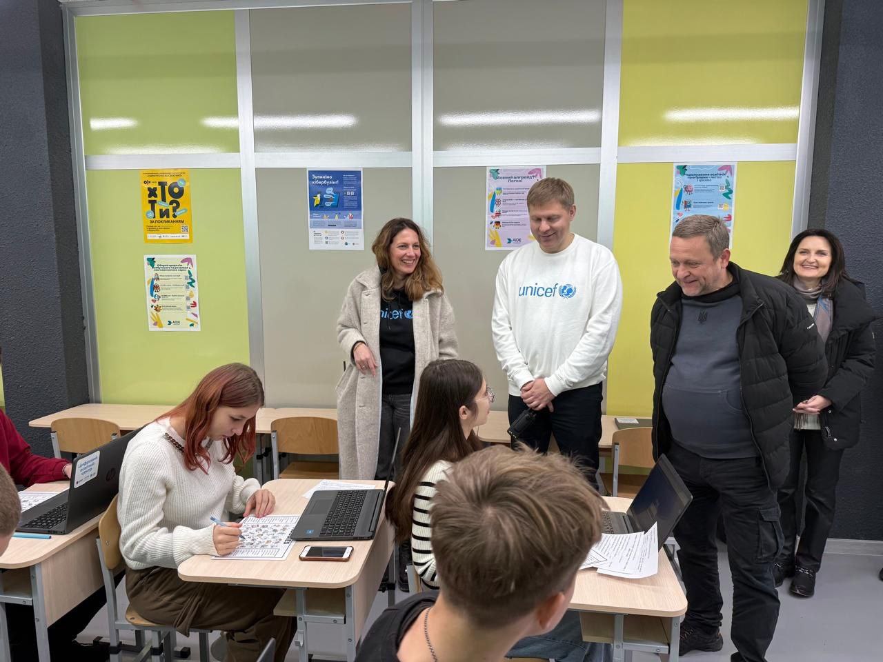 Представники UNICEF та партнери спілкуються з молоддю в сучасному освітньому просторі. Учні працюють за ноутбуками та з навчальними матеріалами, а гості спостерігають за процесом на фоні салатових стін із мотивувальними постерами.