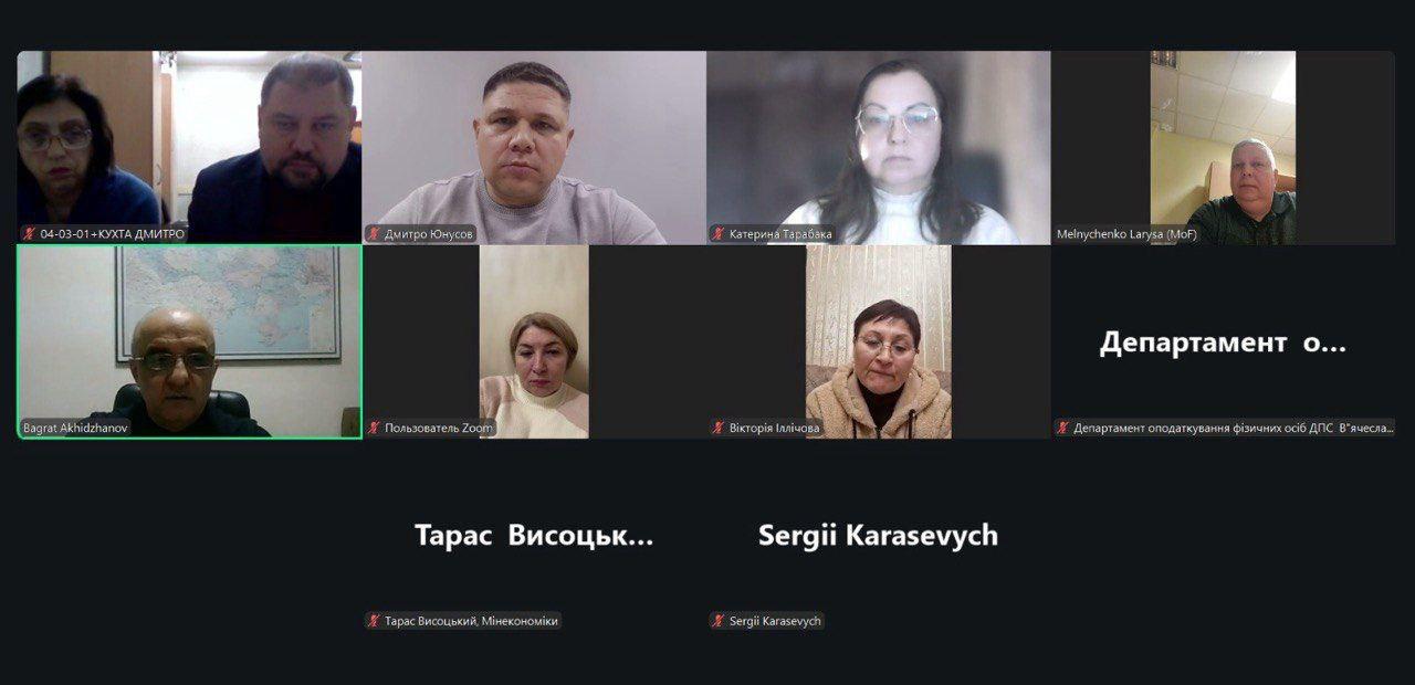 Скриншот онлайн-наради у Zoom, на якому відображено сітку з учасниками. Деякі користувачі ввімкнули відеокамери та знаходяться у домашніх або офісних інтер’єрах, інші присутні лише у форматі аудіо з відображенням імен на темному фоні. Інтерфейс програми містить підписи до відео та іконки вимкнених мікрофонів.