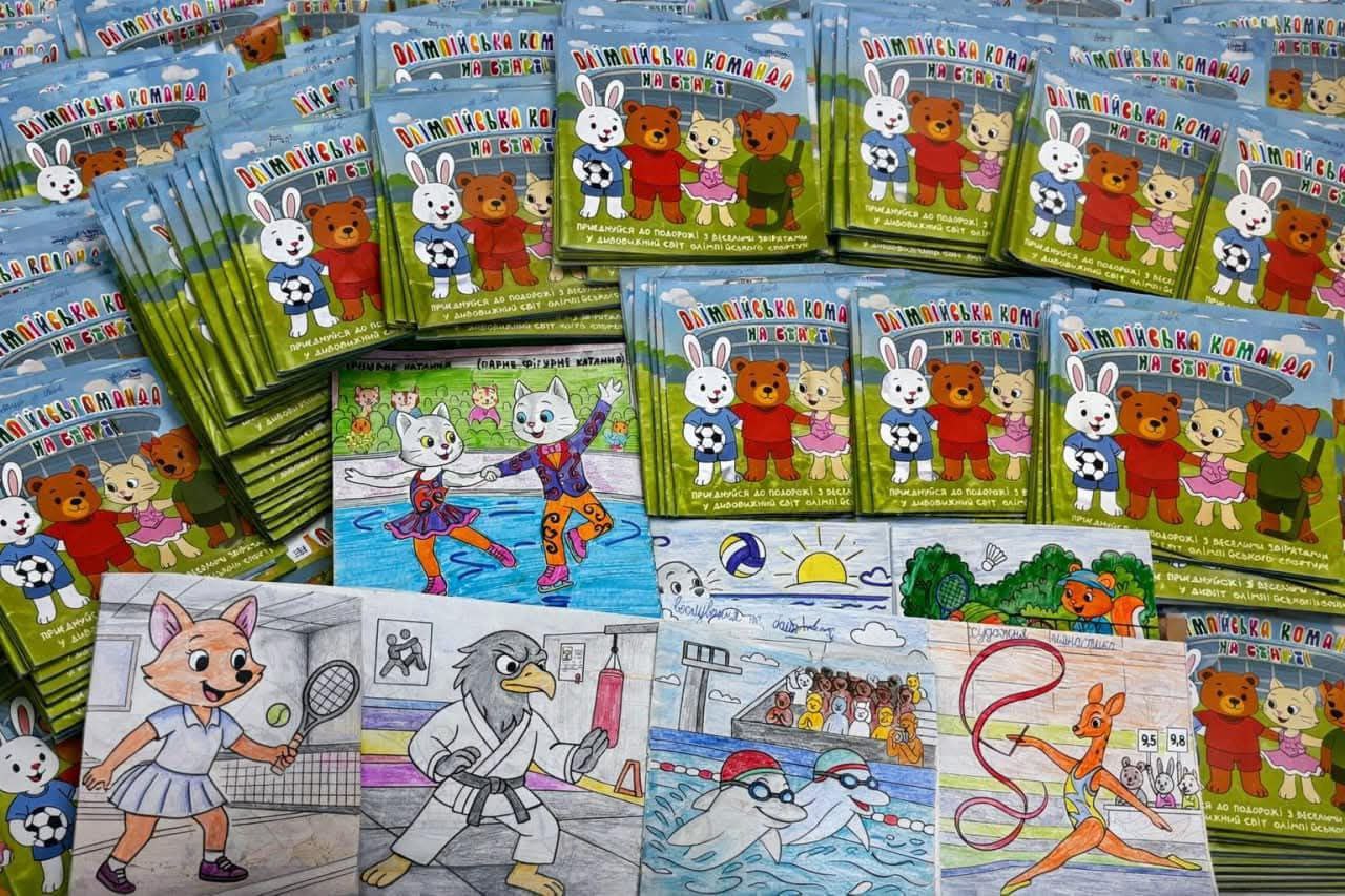 Велика кількість дитячих книжок під назвою «Олімпійська команда на старті», розкладених рядами. На обкладинках та окремих сторінках зображені мультяшні тварини, які займаються різними видами спорту: футболом, фігурним катанням, тенісом, карате, плаванням та художньою гімнастикою.