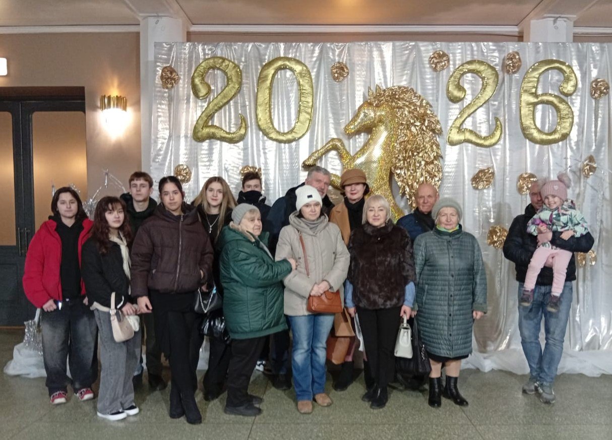 Групове фото людей різного віку, які стоять перед святковою фотозоною. Декорації складаються зі сріблястої завіси, великих золотистих цифр «2026» та фігури золотого коня по центру.