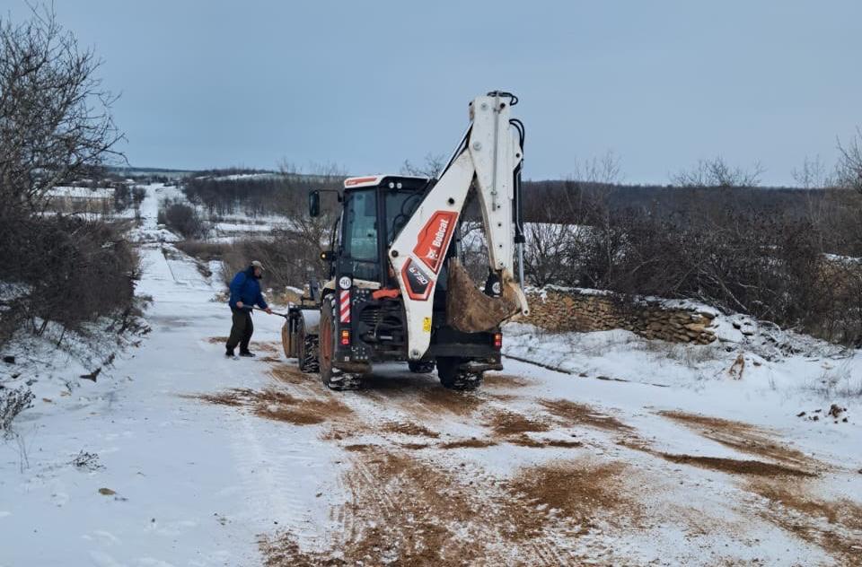Спеціальна техніка розчищає та посипає протиожеледною сумішшю засніжену дорогу між населеними пунктами.
