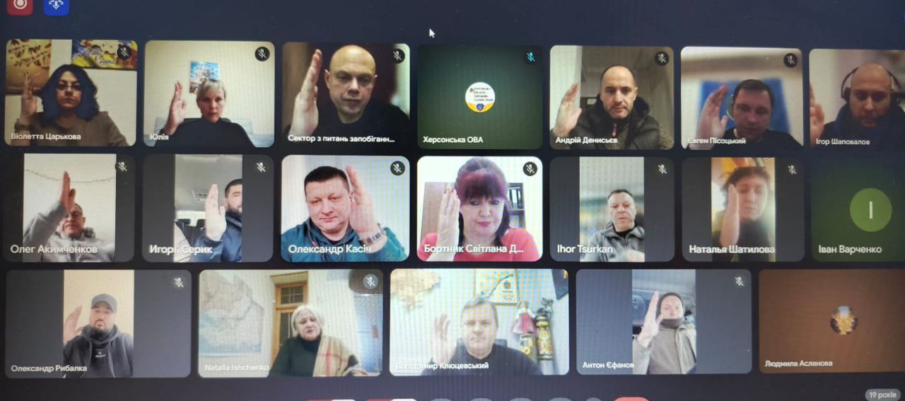 Знімок екрана під час онлайн-наради у форматі відеоконференції. На екрані відображено сітку з вікнами багатьох учасників, більшість з яких підняли руку для голосування або вітання. Під вікнами вказані імена та прізвища присутніх.