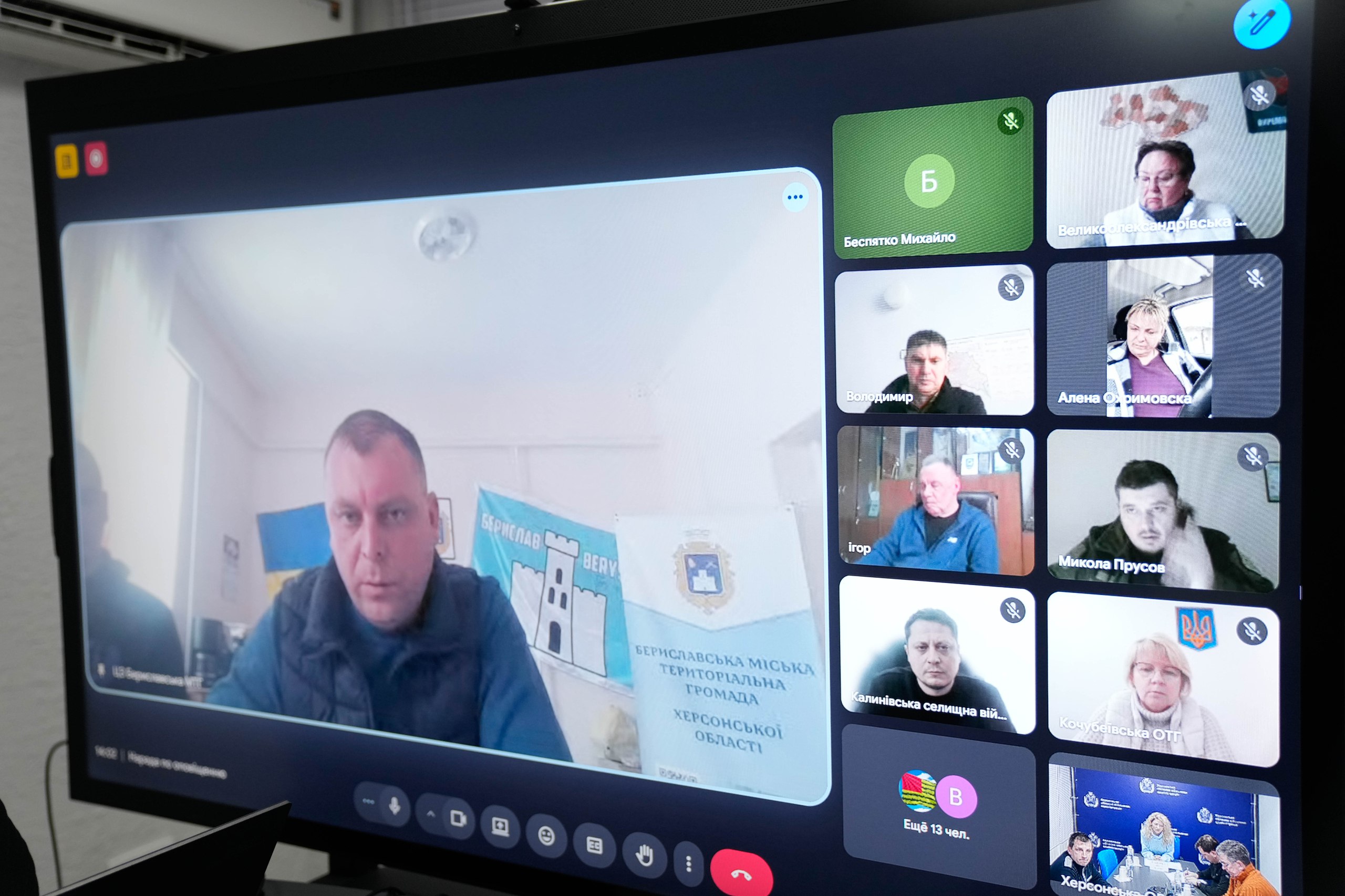 Великий екран монітора, на якому відображено вікно відеоконференції з багатьма учасниками. На головному плані — чоловік, що виступає на тлі прапорів та символіки Бериславської міської територіальної громади. Справа у вертикальній колонці розміщені вікна інших учасників наради.