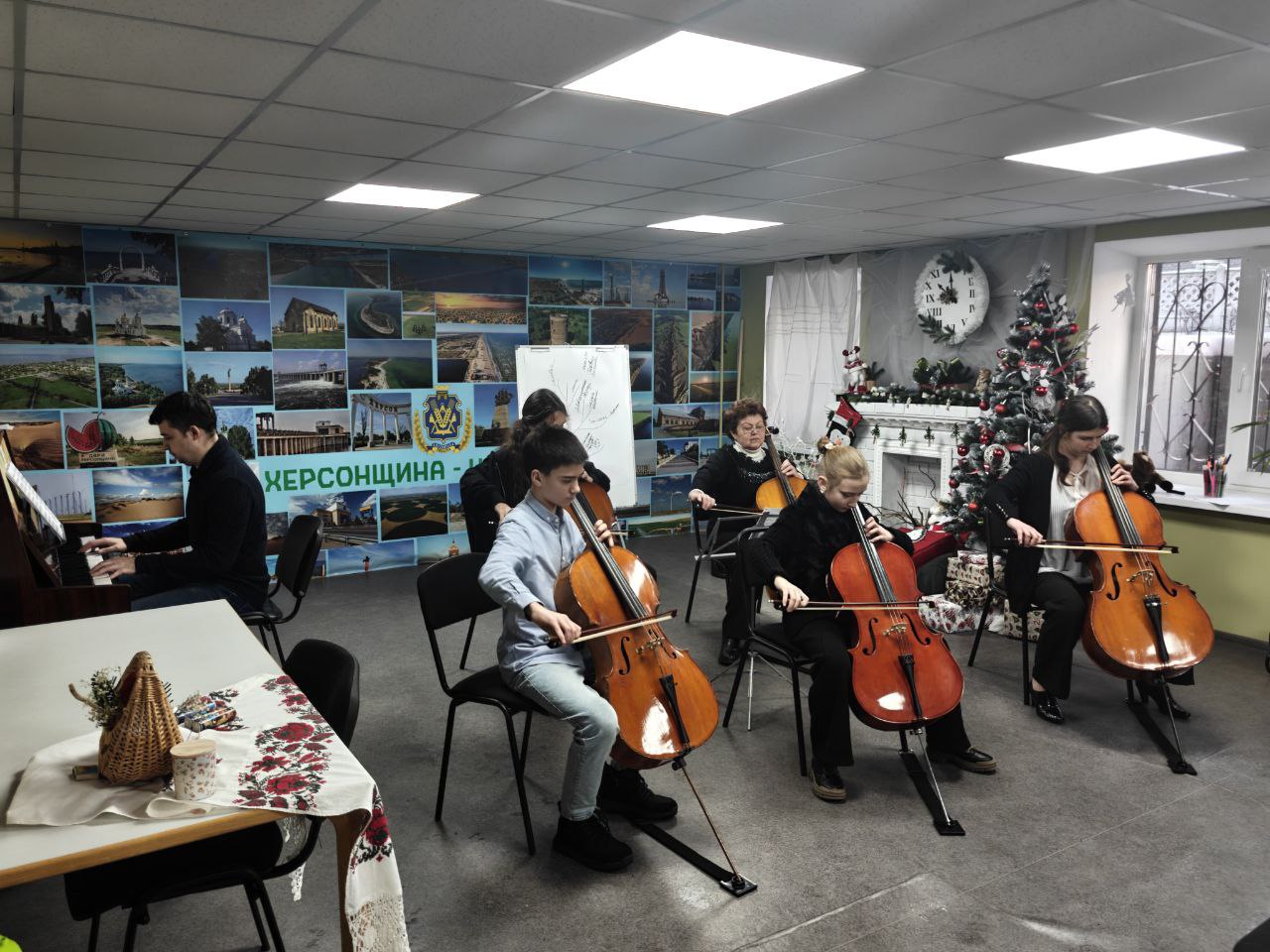 Ансамбль із п'ятьох віолончелістів та піаніста виступає в затишному приміщенні. На задньому плані стіна прикрашена фотоколажем із краєвидами Херсонщини та написом «Херсонщина — це Україна». У кутку кімнати стоїть святкова ялинка та декоративний камін.