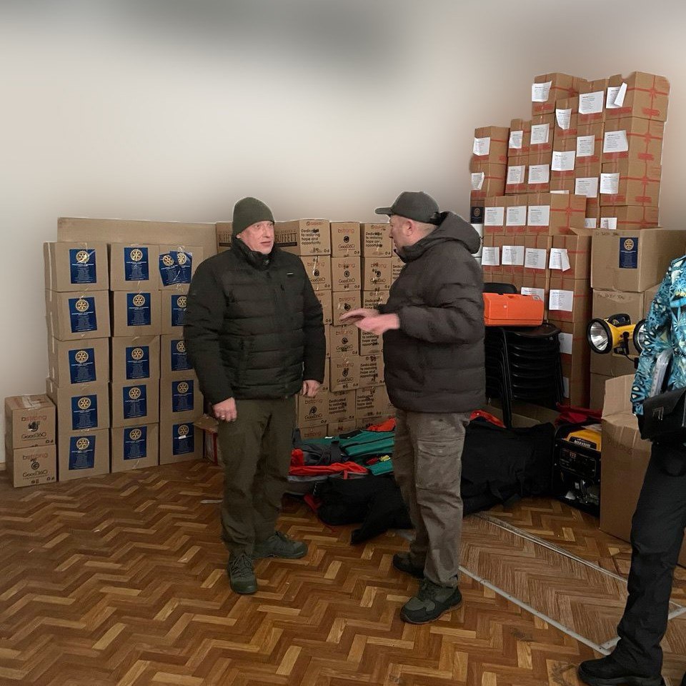 Двоє чоловіків спілкуються у приміщенні, заповненому високими стосами коробок із гуманітарною допомогою.